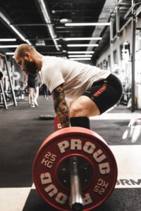 how to do squats - man in white t-shirt and black shorts carrying red and black barbell