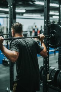 how to do squats -- man in black t-shirt carrying barbell